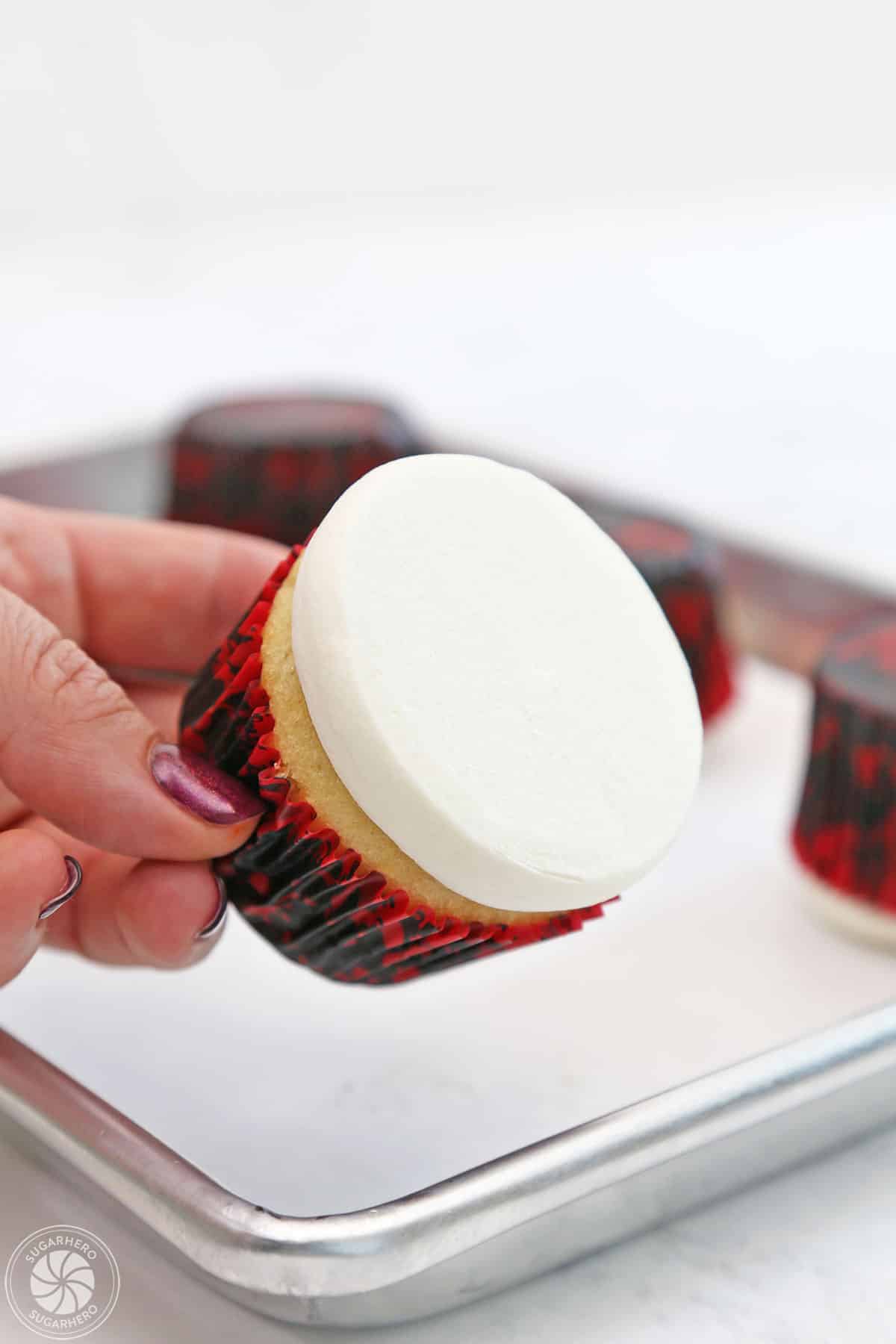 Hand showing a cupcake with smooth, flattened buttercream on top.