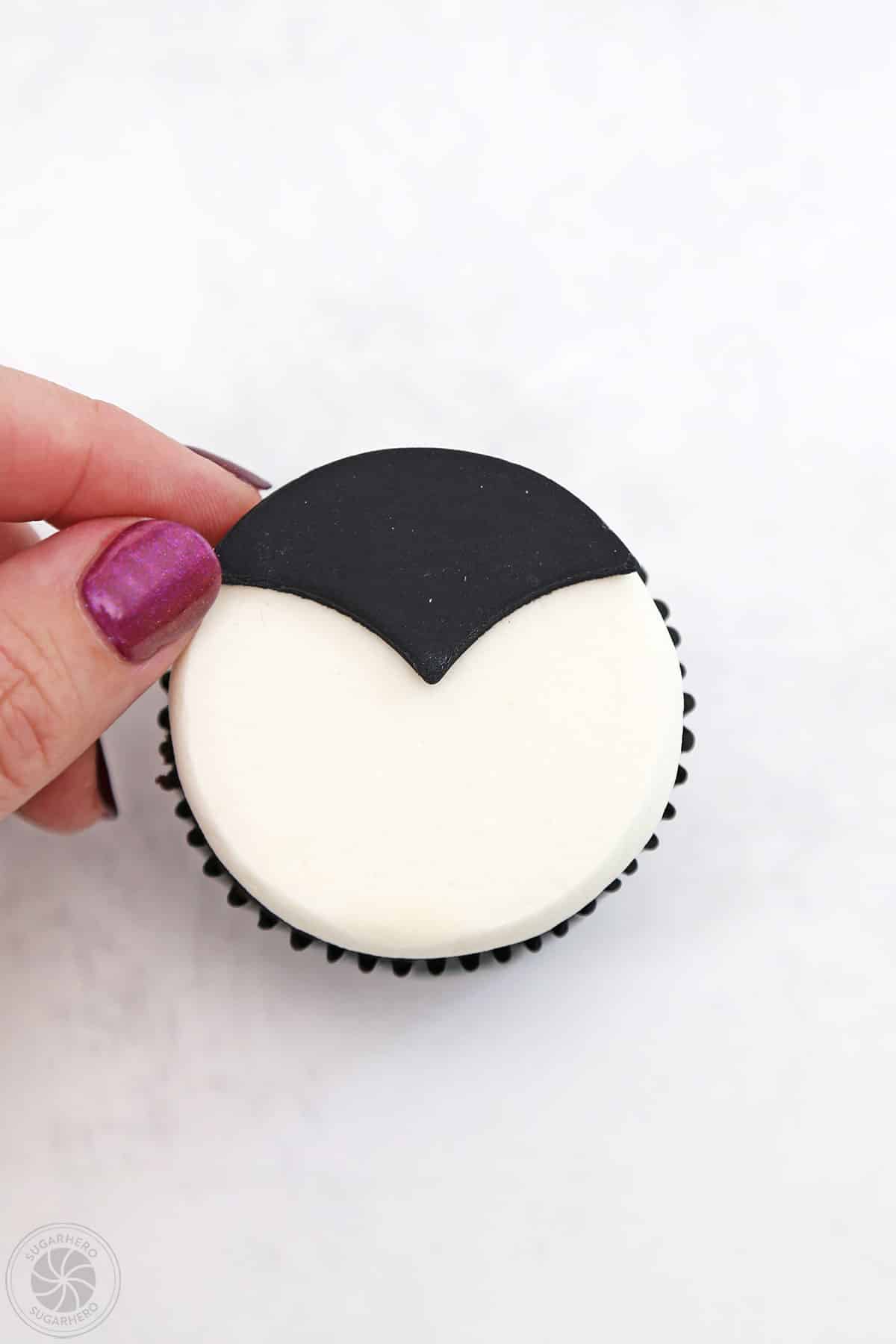 Hand placing black fondant vampire hair on a cupcake.
