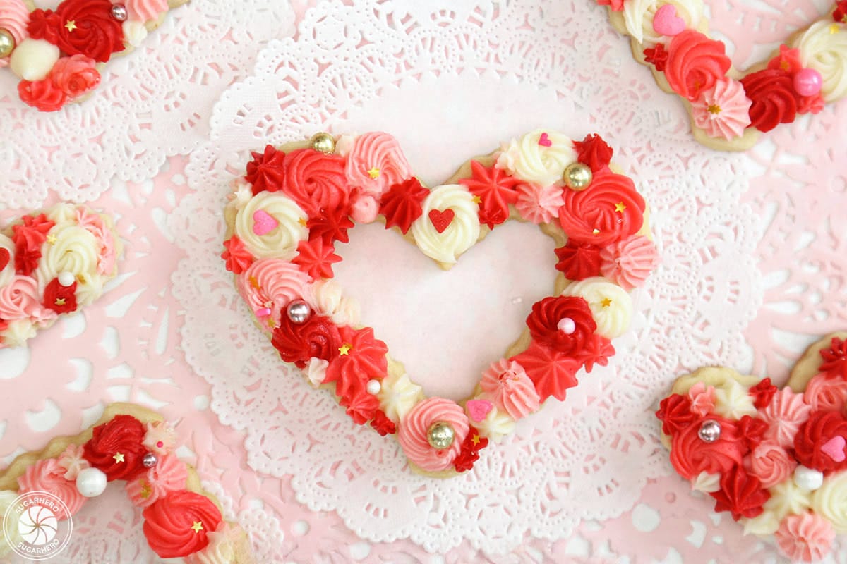 Overhead shot of heart-shaped sugar cookie decorated with piped buttercream frosting, on a white doily.