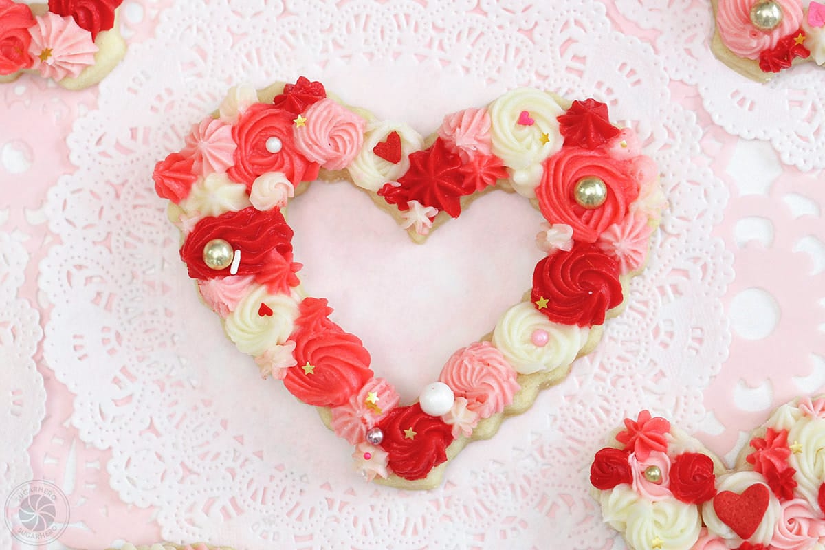 Close-up of a sugar cookie cut into a heart shape, topped with different colors of piped buttercream.