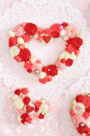 Close-up of a frosted sugar cookie decorated with piped red, pink, and white buttercream and sprinkles.