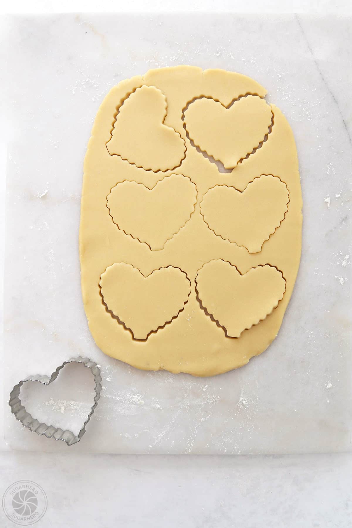 Sugar cookie dough rolled out on a marble slab with hearts cut out of it.