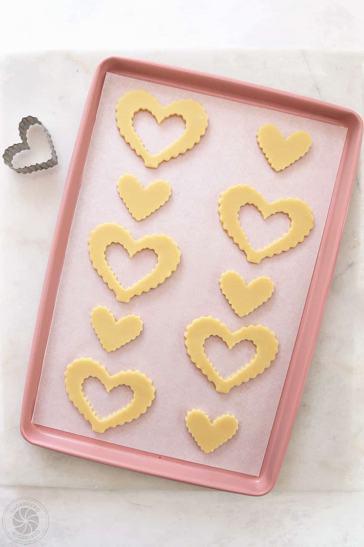 Cut-out sugar cookies on a pink baking sheet covered with parchment.