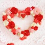 Close-up of a heart-shaped sugar cookie with red, pink, and white buttercream and sprinkles.