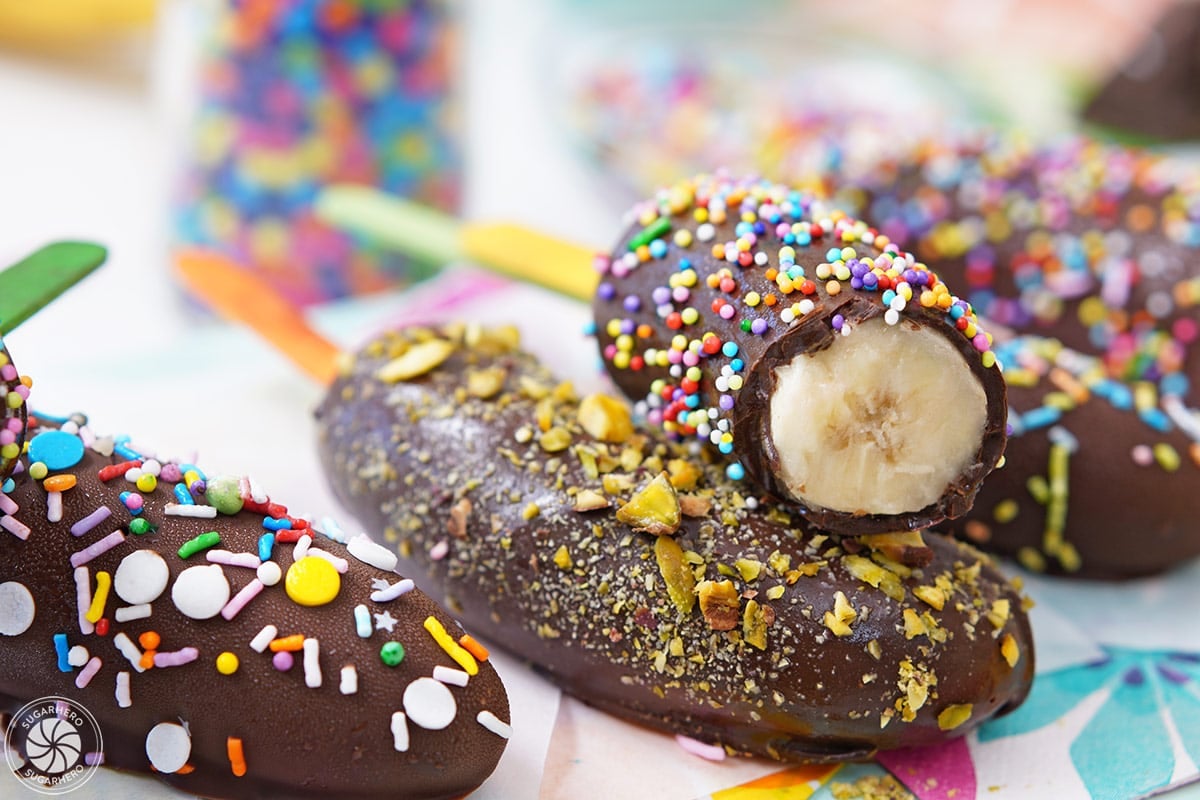 Chocolate-Dipped Frozen Bananas | SugarHero.com A row of chocolate-dipped frozen bananas with one cut to show the center.