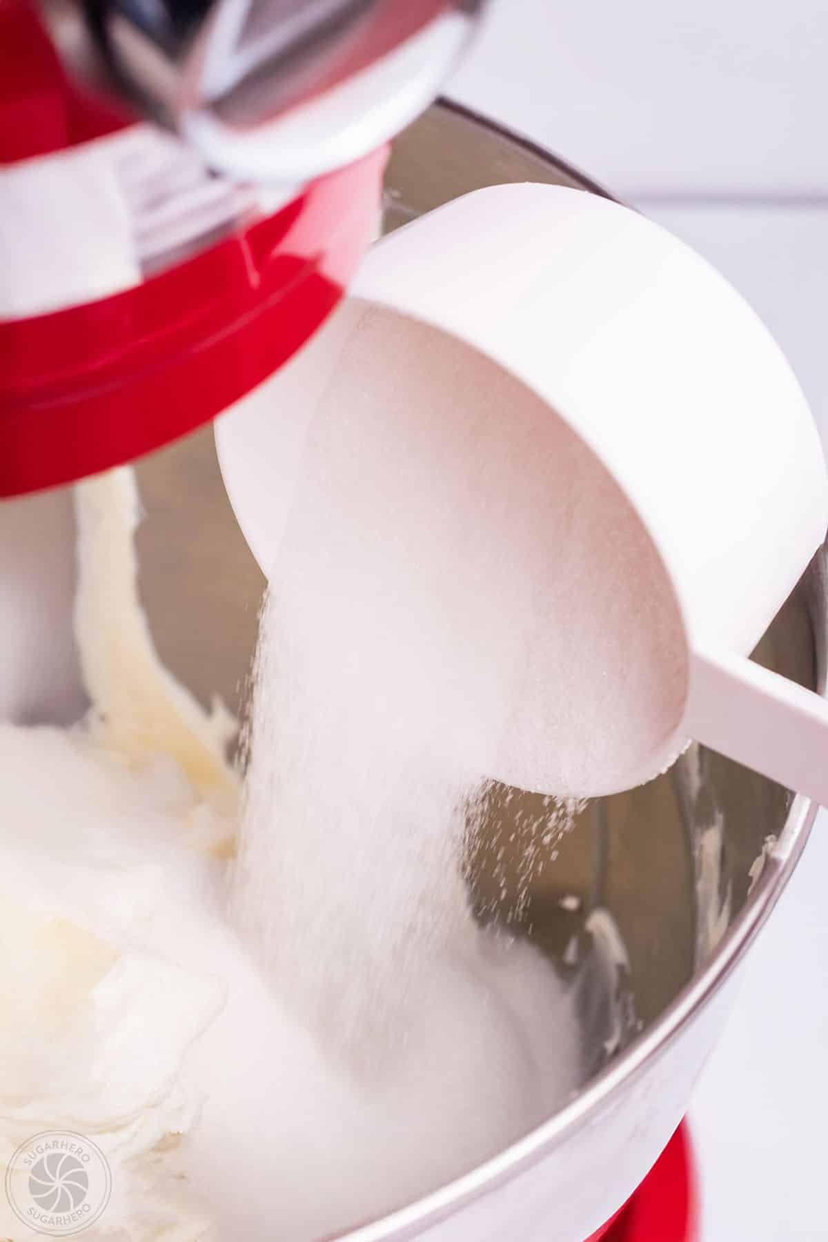 Sugar being poured into a mixer with cream cheese.