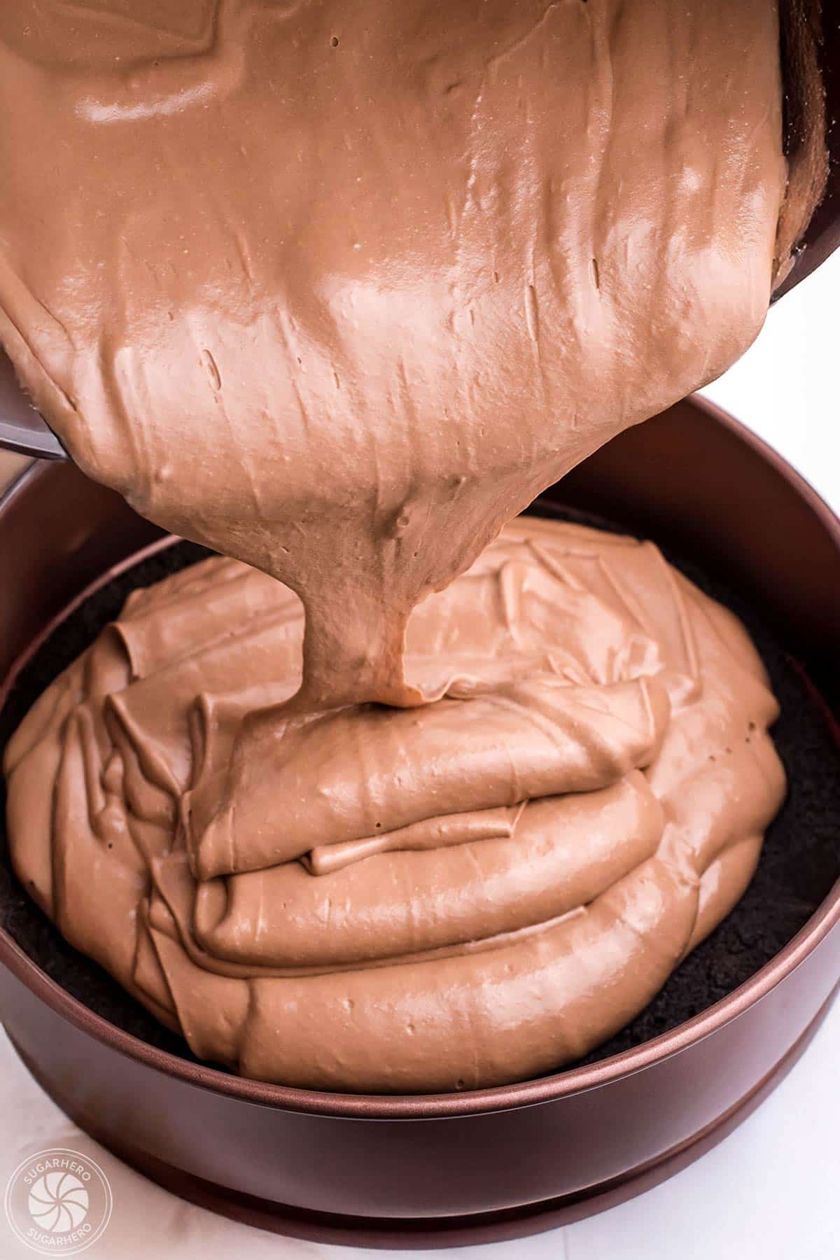 Pouring chocolate cheesecake filling into a springform pan.