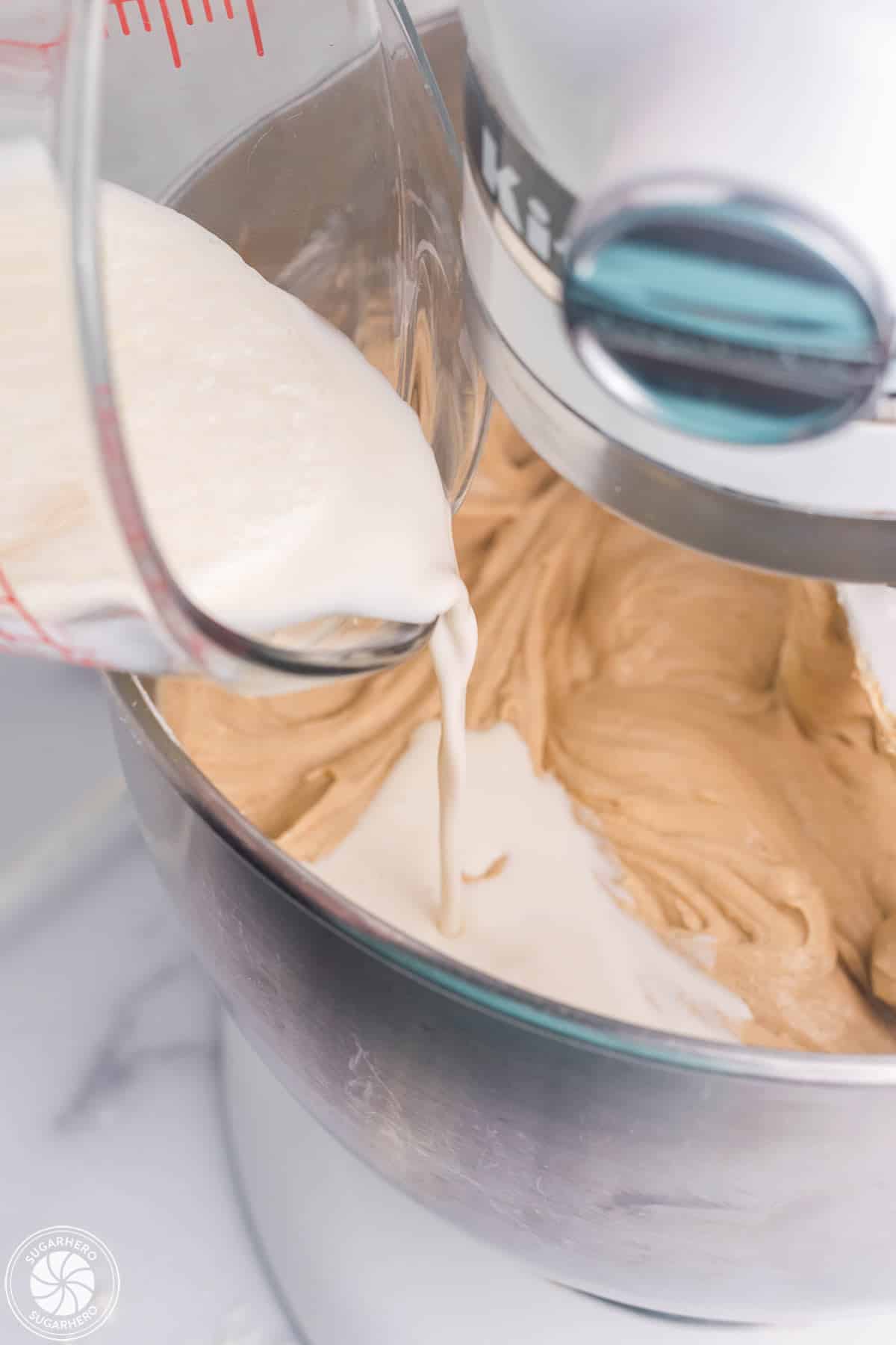 Pouring cream into a mixer bowl full of gingerbread cheesecake filling.
