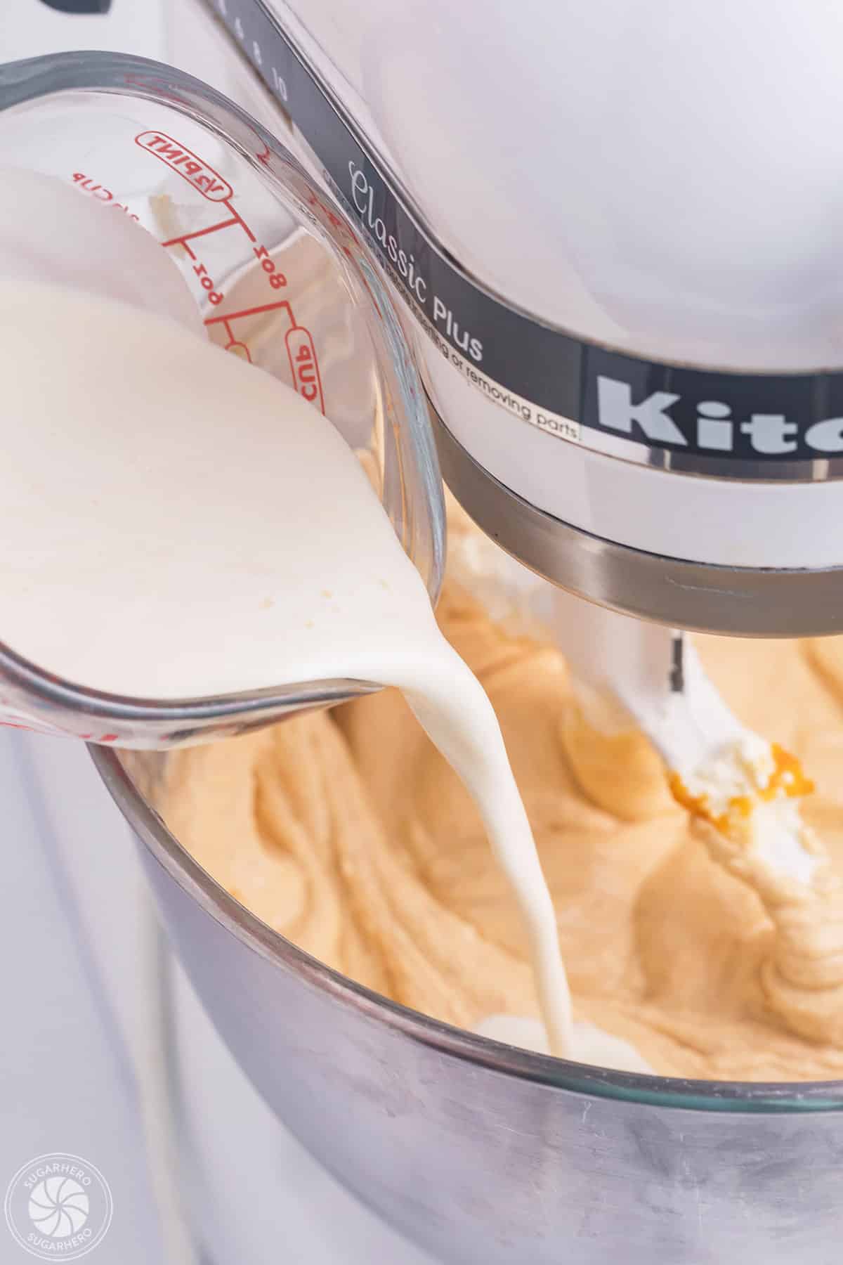 Pouring cream into a mixer filled with pumpkin spice cheesecake filling.