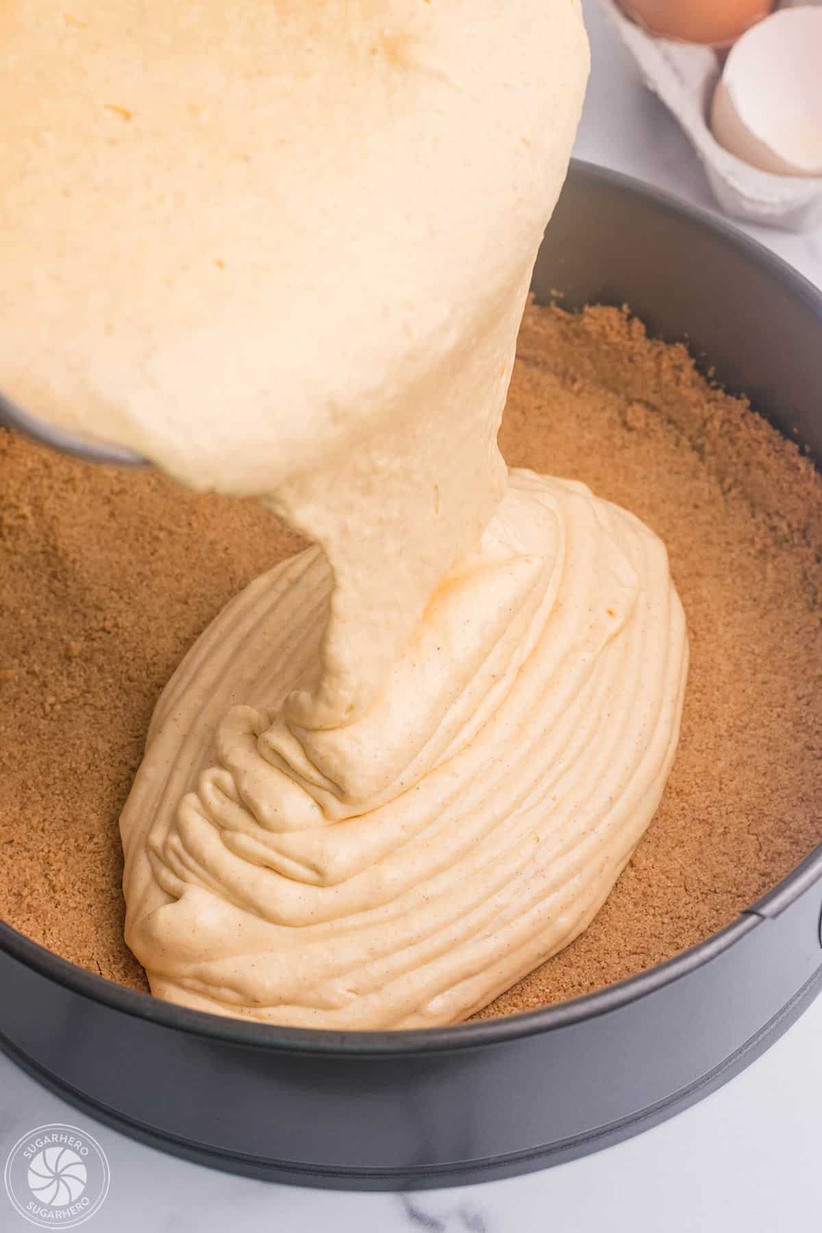 Pumpkin spice cheesecake filling being poured over a graham cracker crust.
