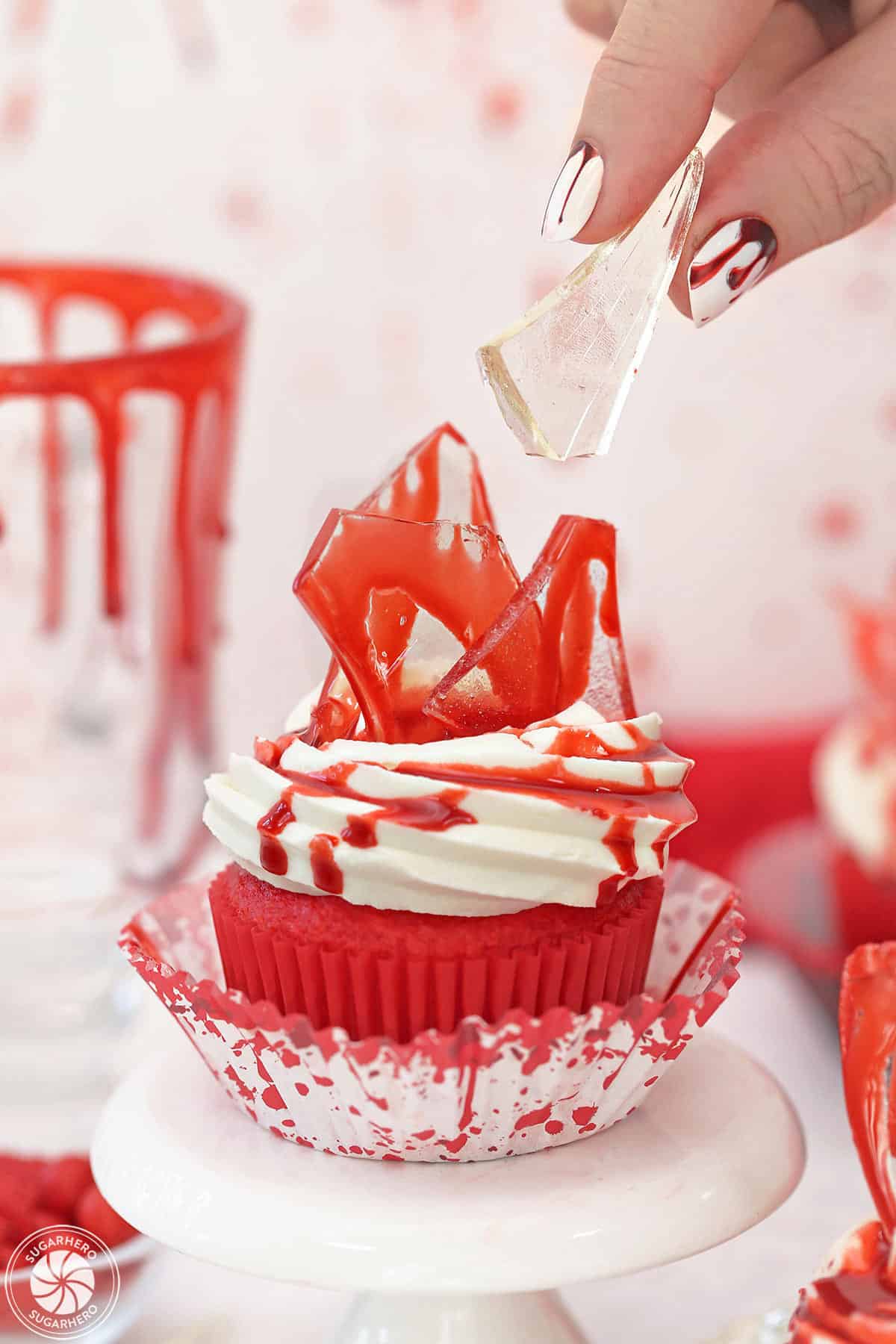 Hand placing a piece of edible glass on top of a bloody glass cupcake.