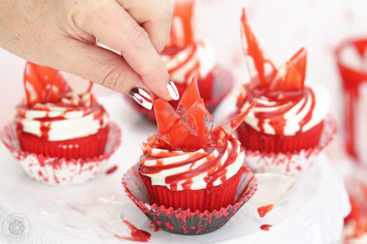 Hand placing a piece of glass on top of a bloody glass cupcake.