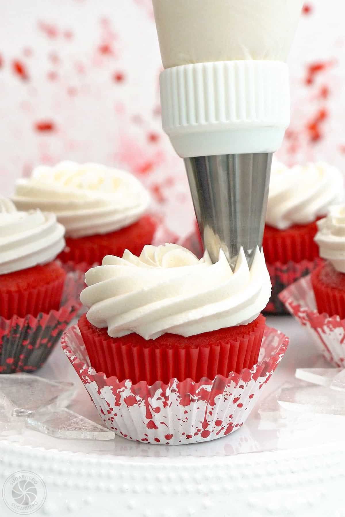 White frosting being piped onto a red velvet cupcake.