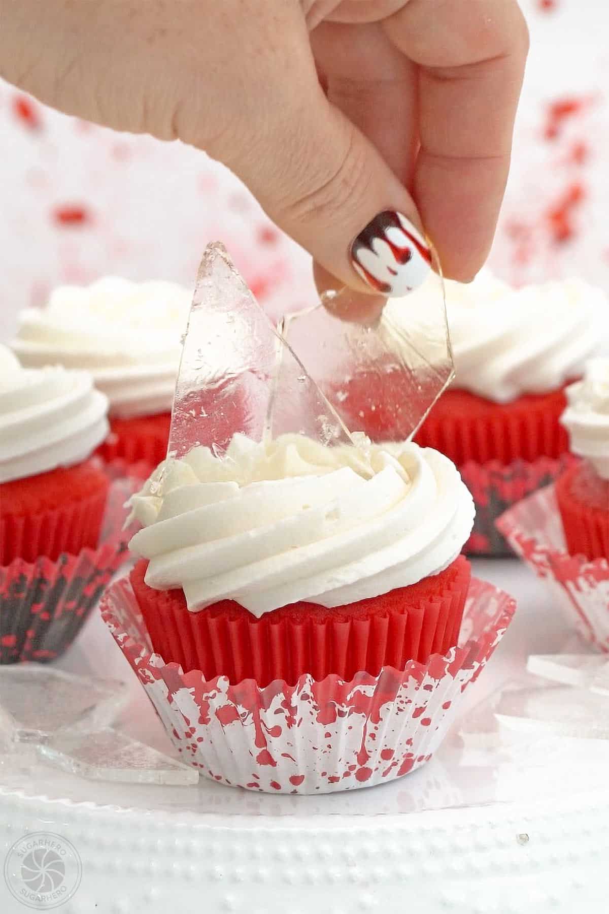 Hand placing edible sugar glass on top of a cupcake.