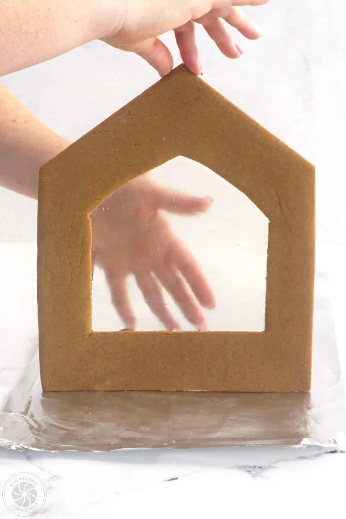 Hand showing a gingerbread house panel with a candy glass window.