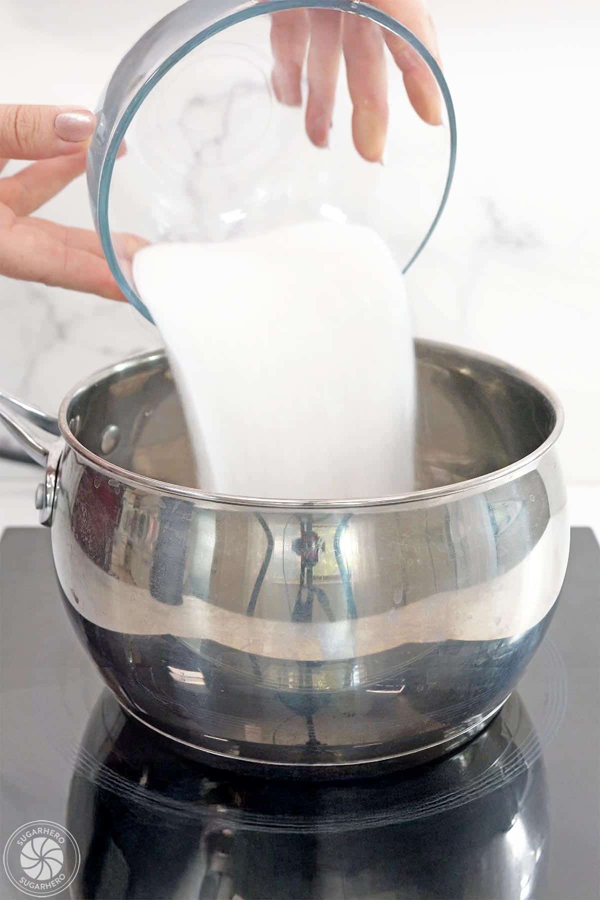Hand pouring sugar into a pot.