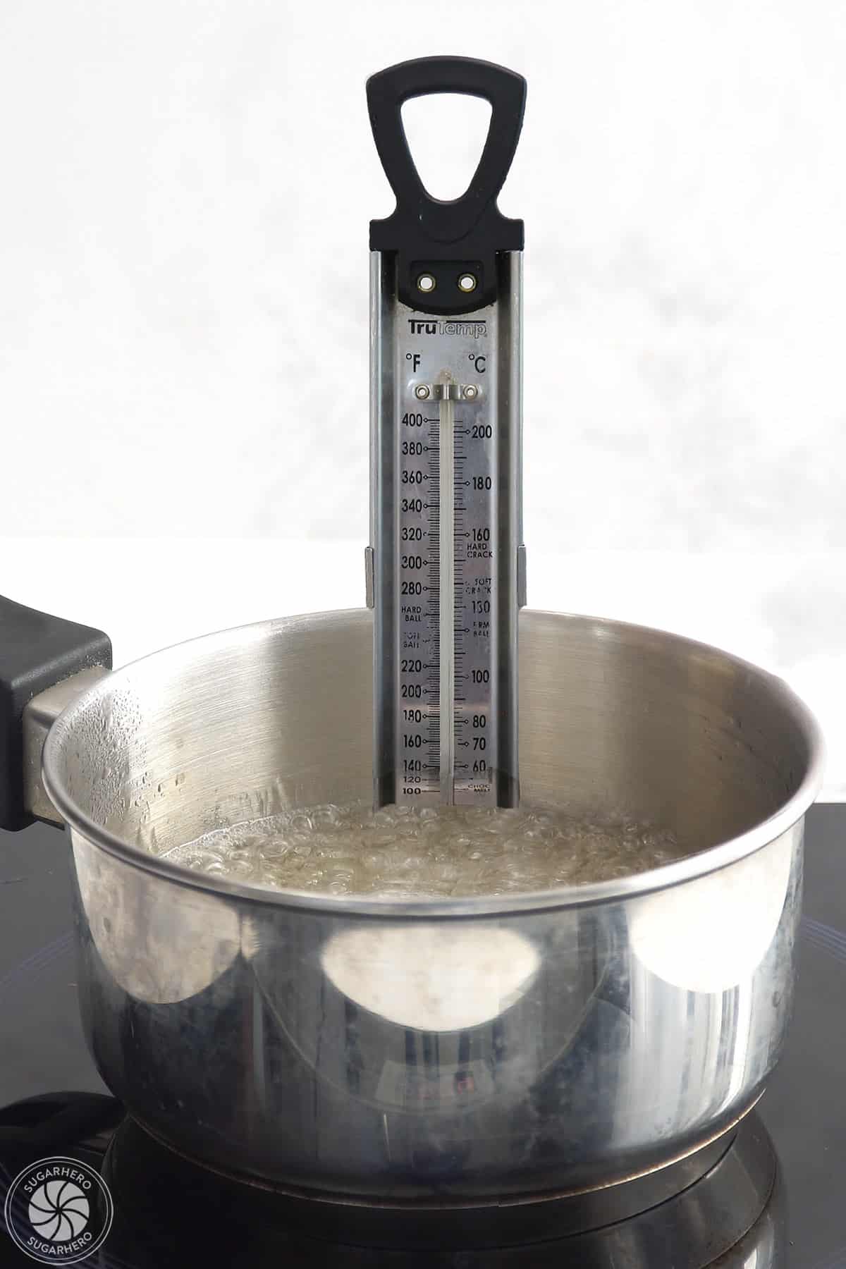 A pot with boiling sugar syrup with a candy thermometer inserted.