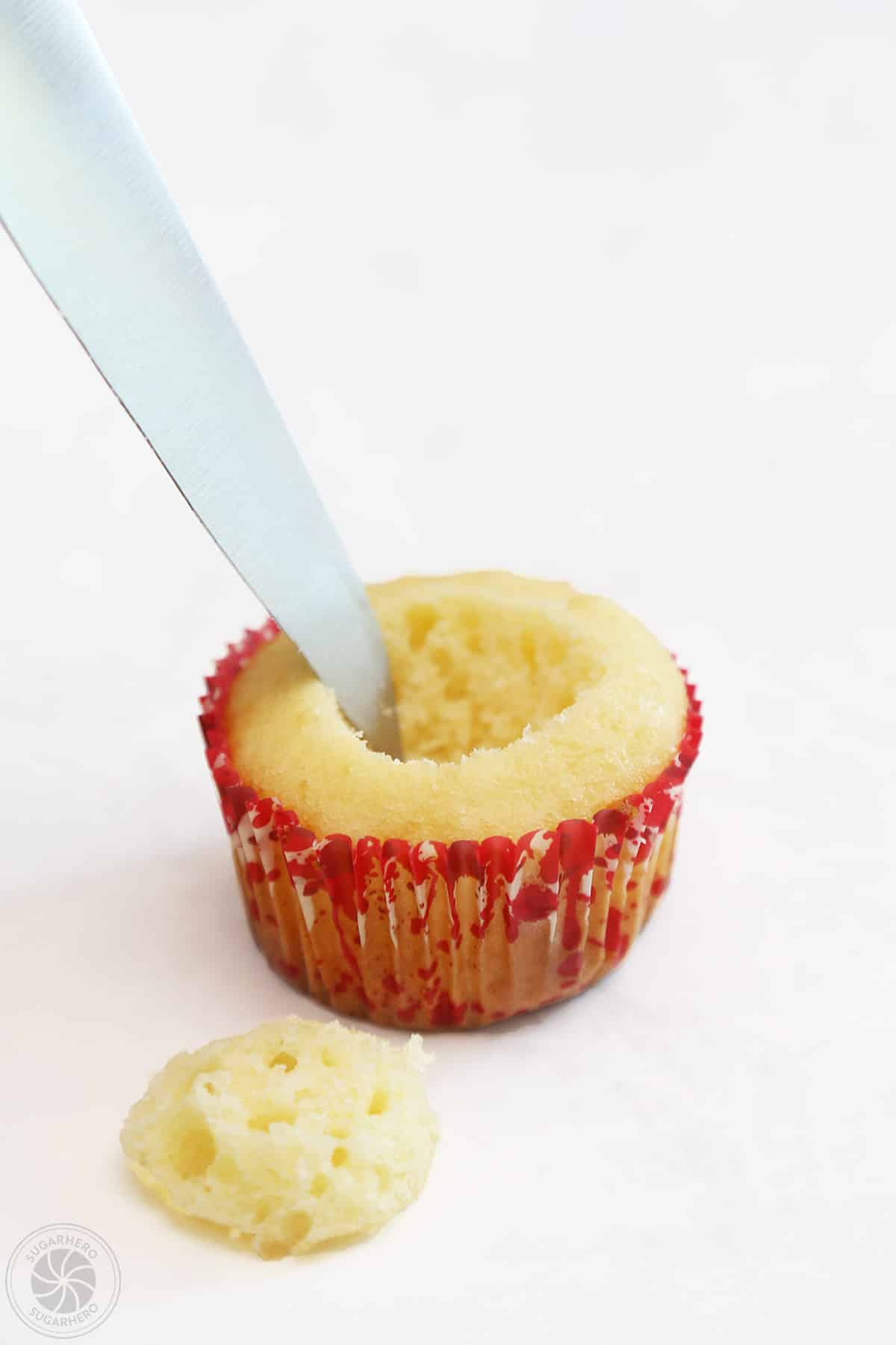 Using a knife to hollow out the center of a cupcake.