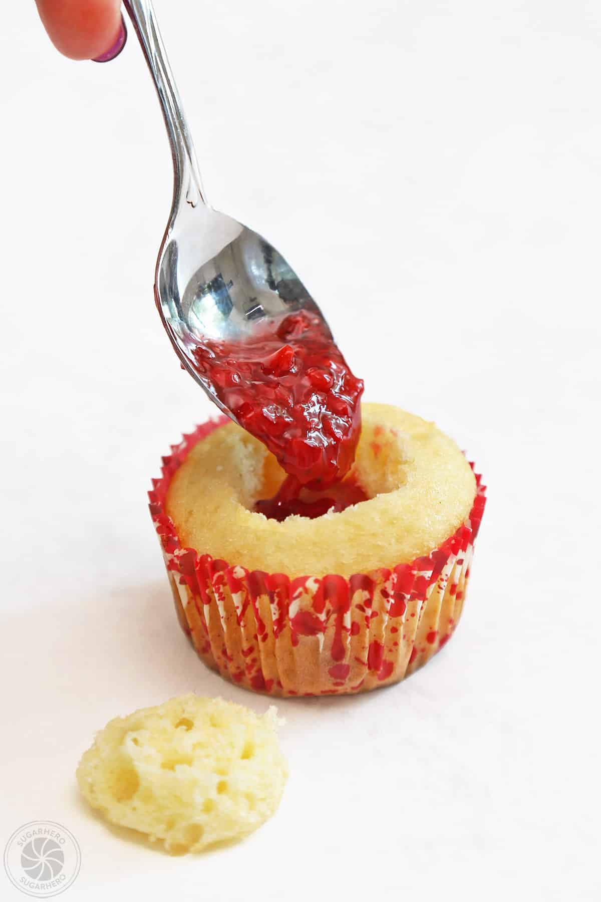 A cupcake being filled with red cherry filling.