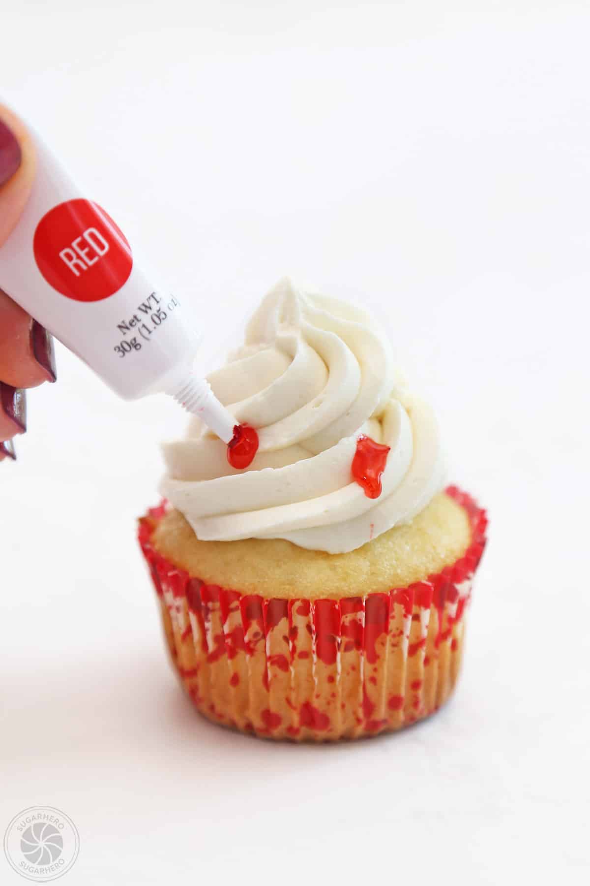 Hand squeezing red gel on a cupcake to look like a vampire bite.
