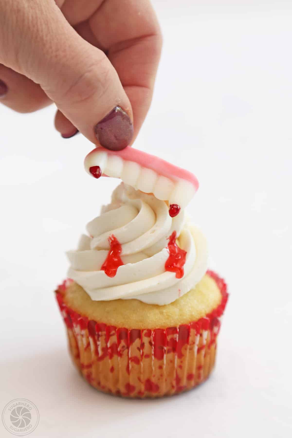 Hand placing vampire teeth on a vampire bite cupcake.
