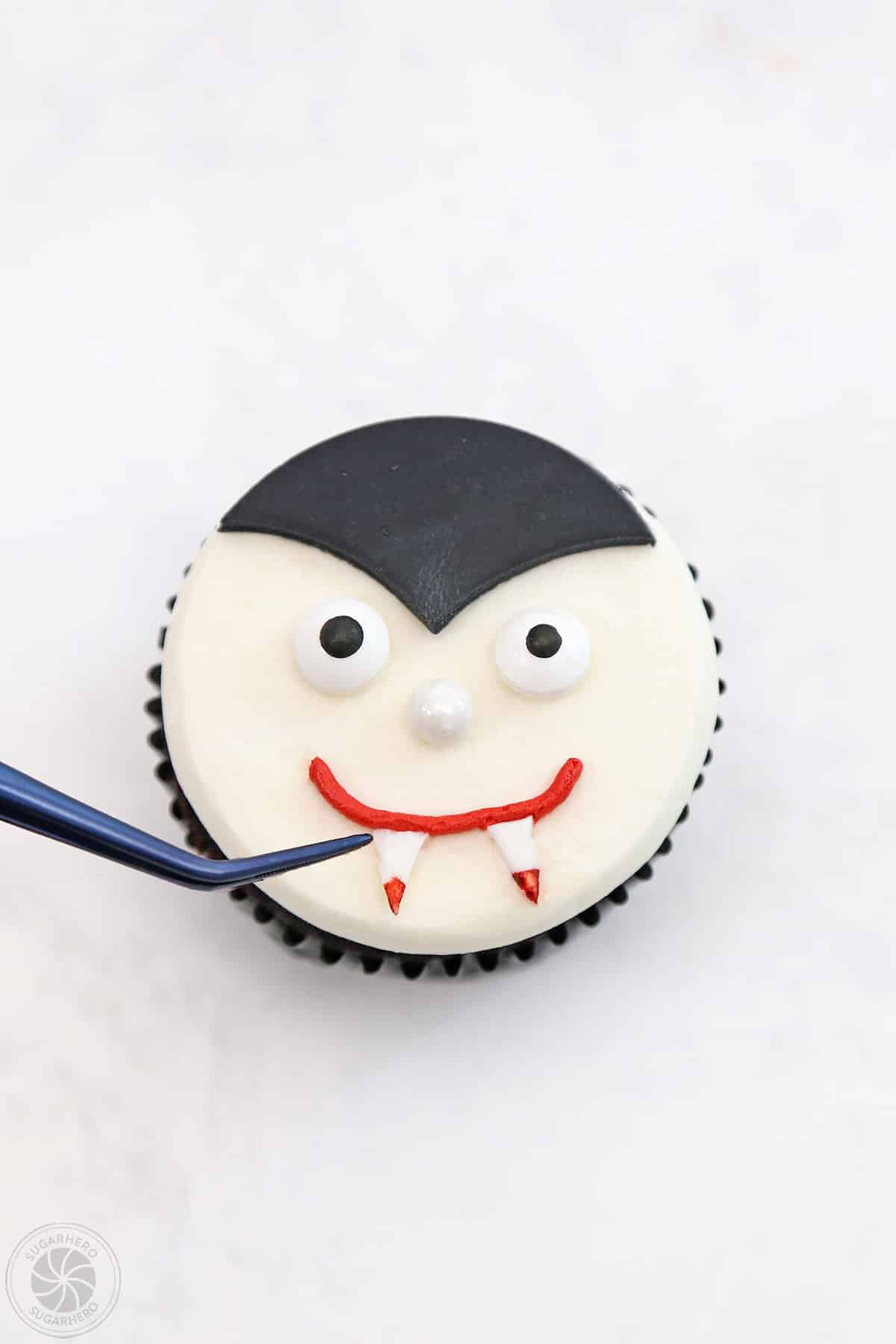 Adding bloody fondant teeth to the top of a vampire cupcake.