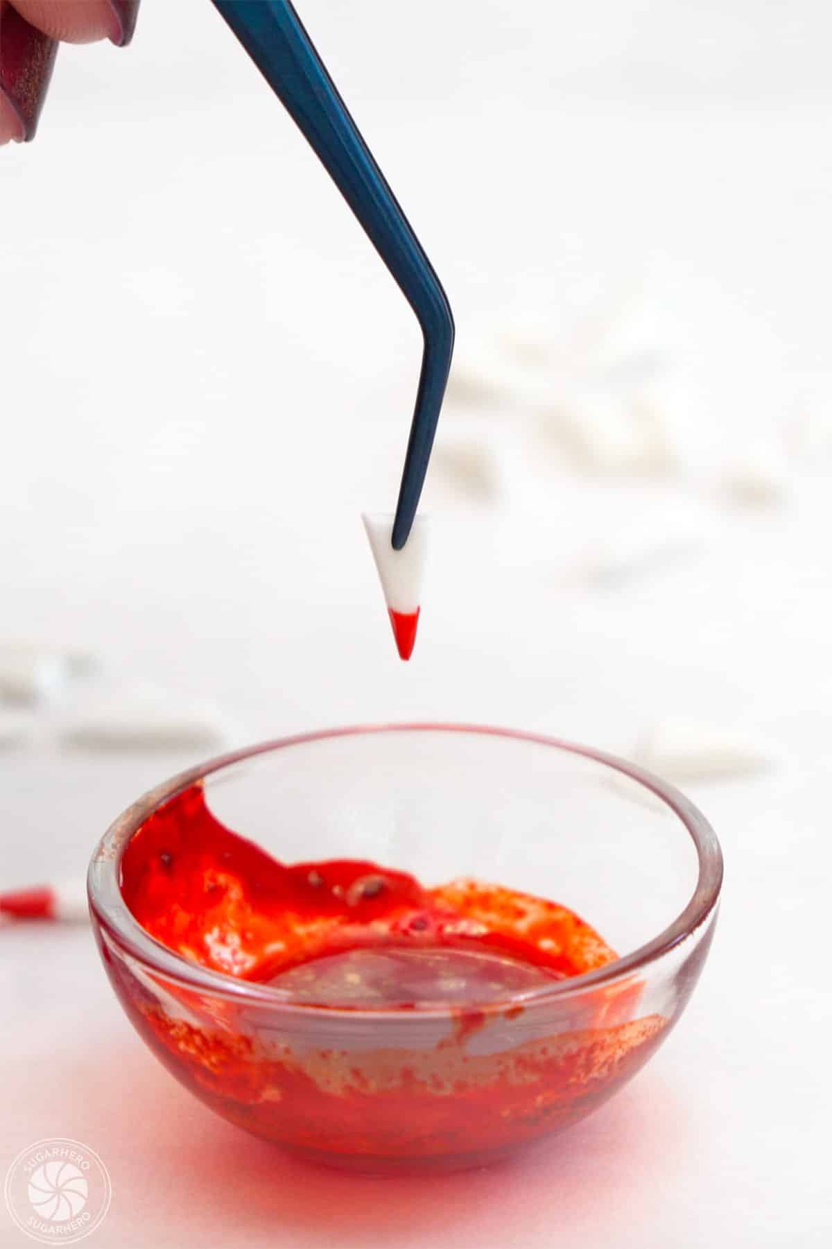 Dipping a triangle of fondant into red food color to resemble vampire teeth.