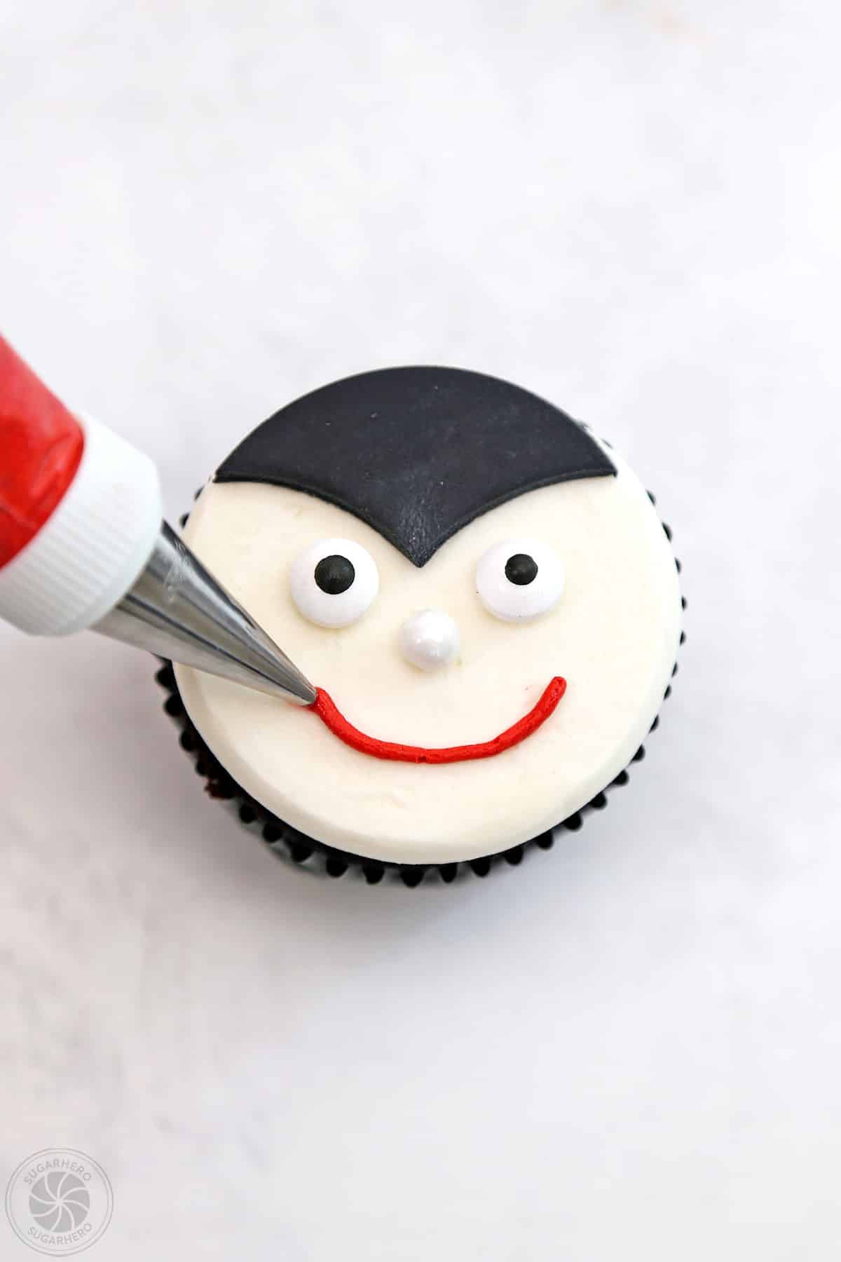 Piping a red smile onto a vampire cupcake.