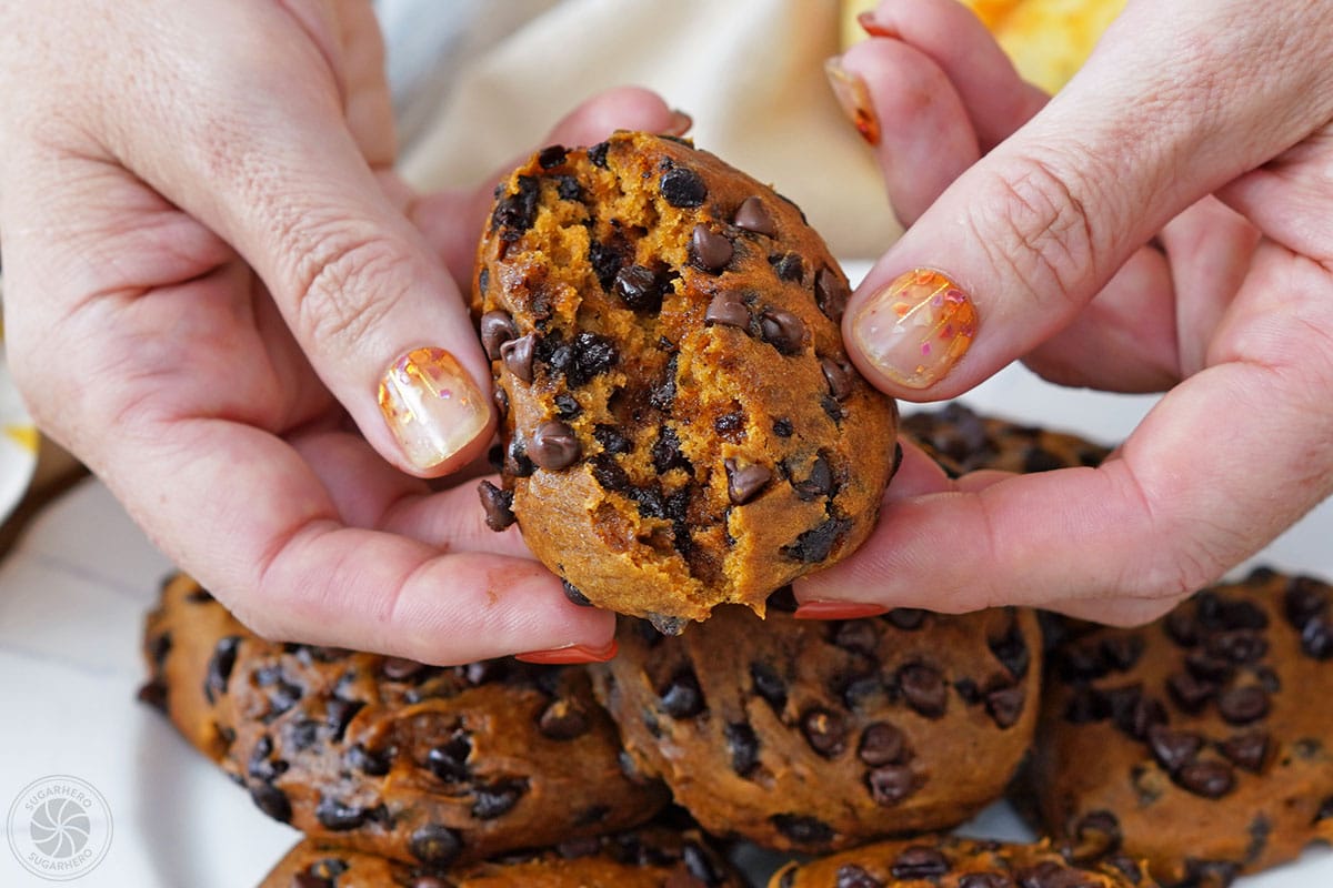 Hand breaking open a baked pumpkin chocolate chip cookie.