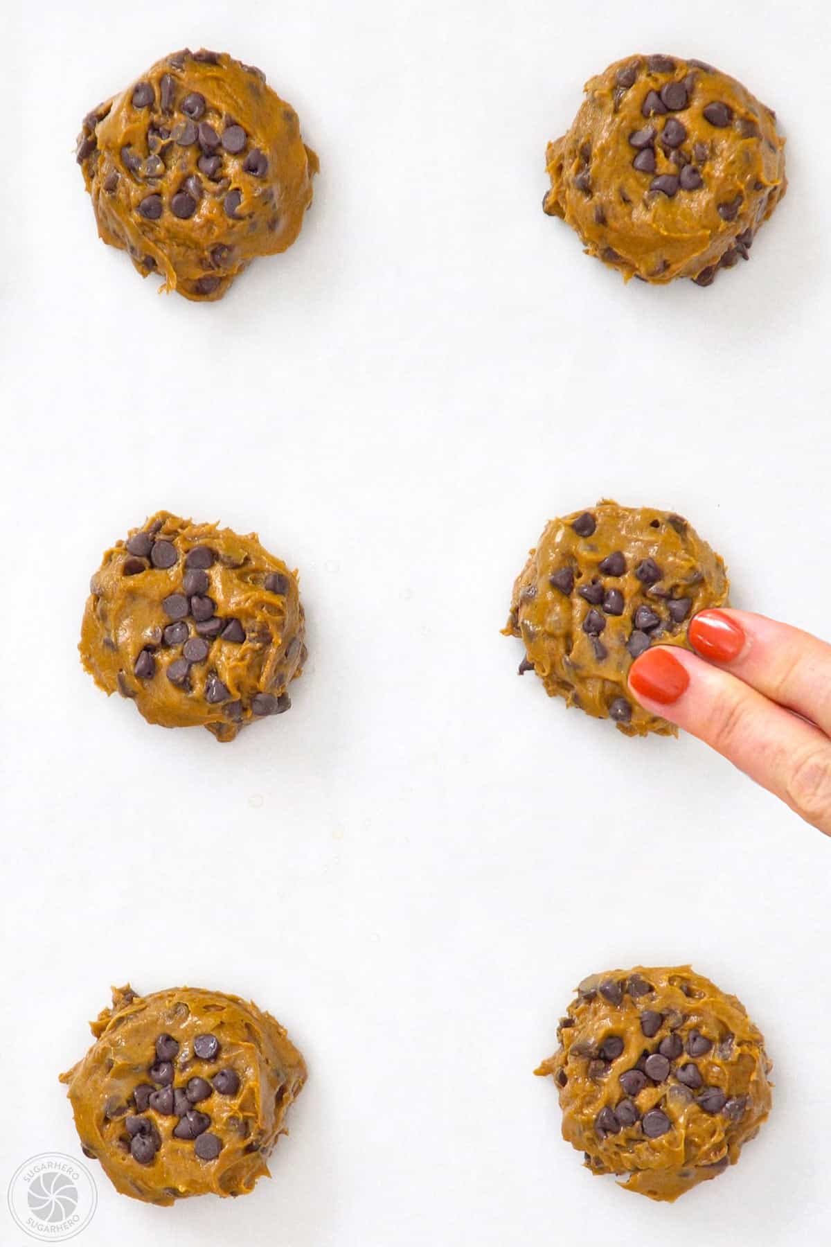 Pressing mini chips onto the top of pumpkin chocolate chip cookies and smoothing out the edges.