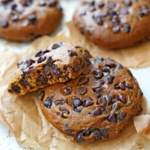 Close up of two pumpkin chocolate chip cookies that are overlapping with a bite removed from top cookie.