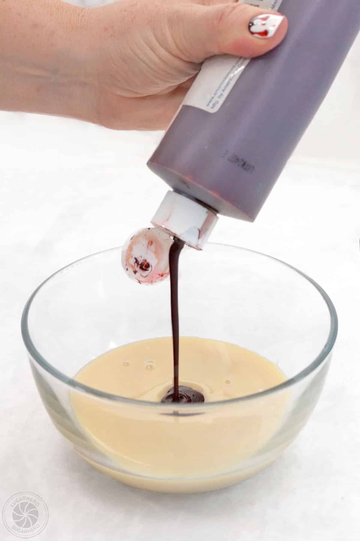 Adding red food coloring to a bowl of sweetened condensed milk.