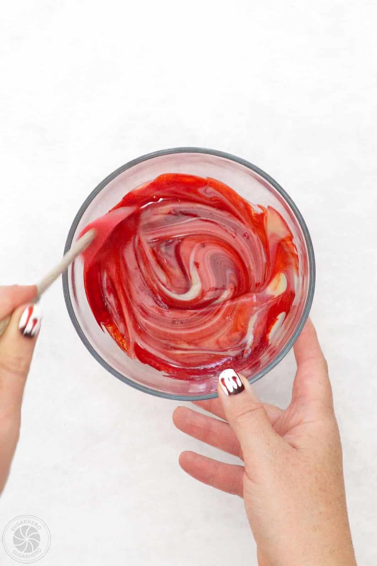 Stirring red food coloring into a bowl of sweetened condensed milk.