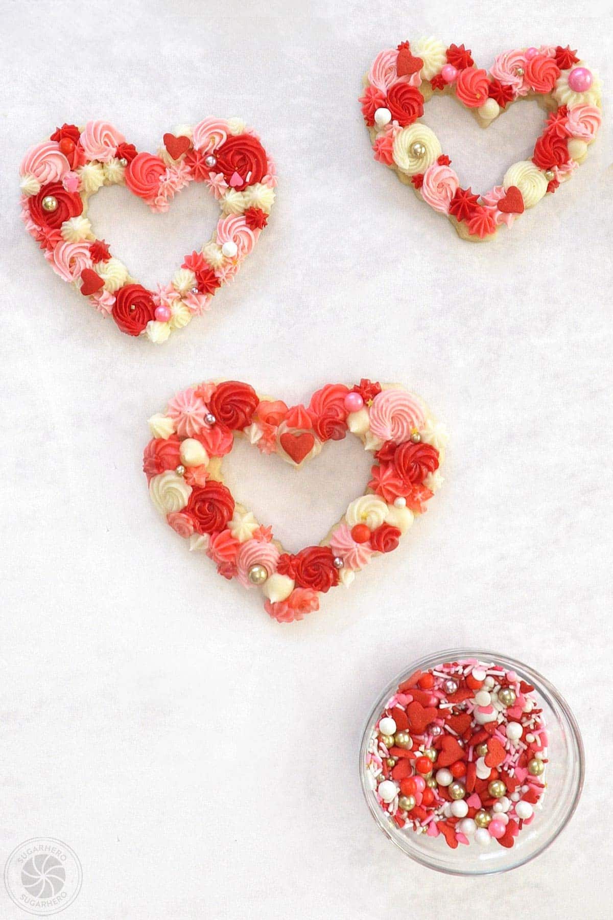 Three decorated buttercream sugar cookies next to a bowl of sprinkles.