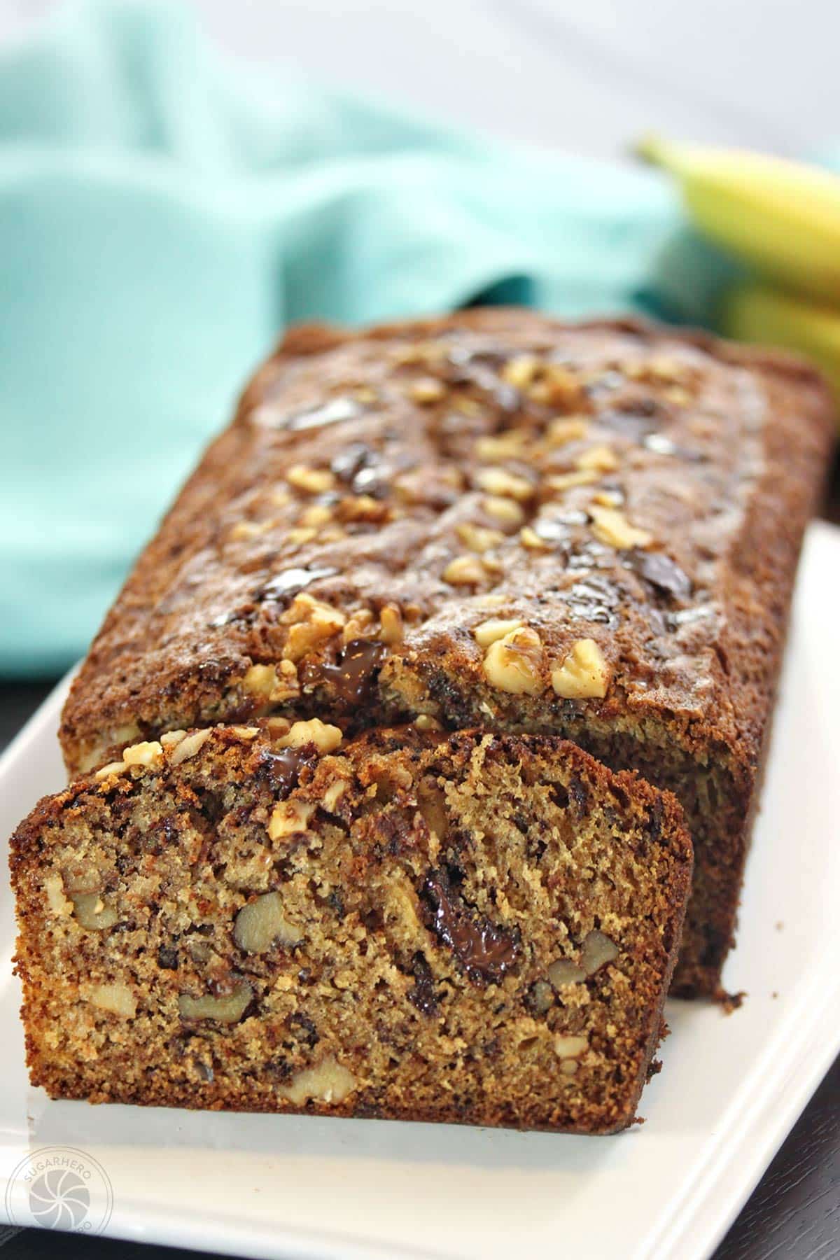 The ultimate banana bread - made with coconut oil and lots of chocolate chunks! | From SugarHero.com A loaf of banana bread on a white rectangular platter.