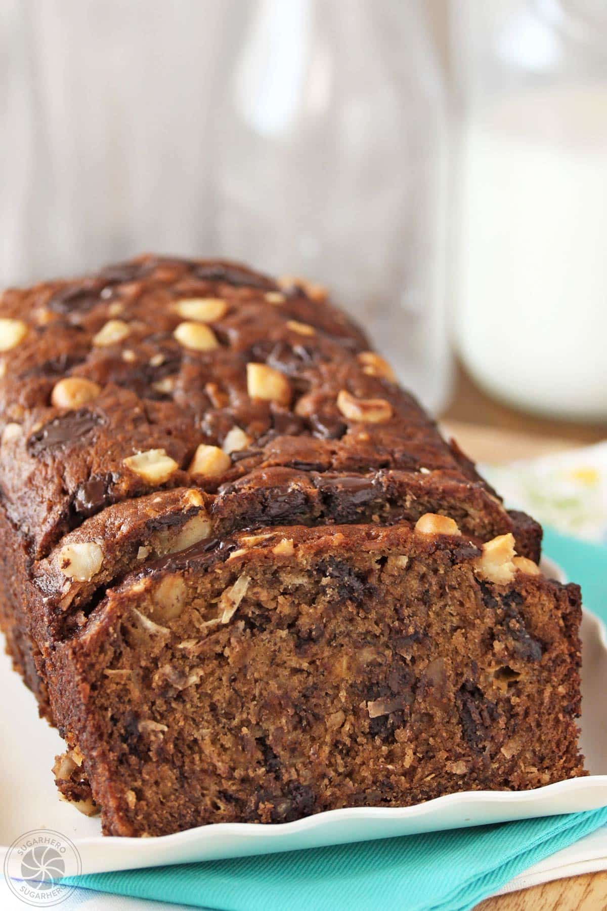 A loaf of banana coconut macadamia nut bread on a white plate with a few slices cut off the end.