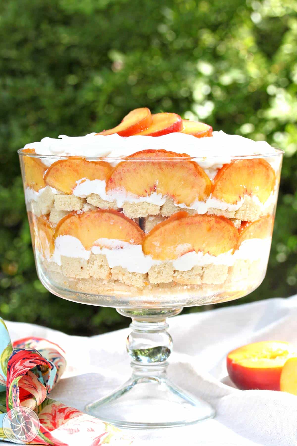 A peaches and cream trifle on a white table cloth with greenery in the background.