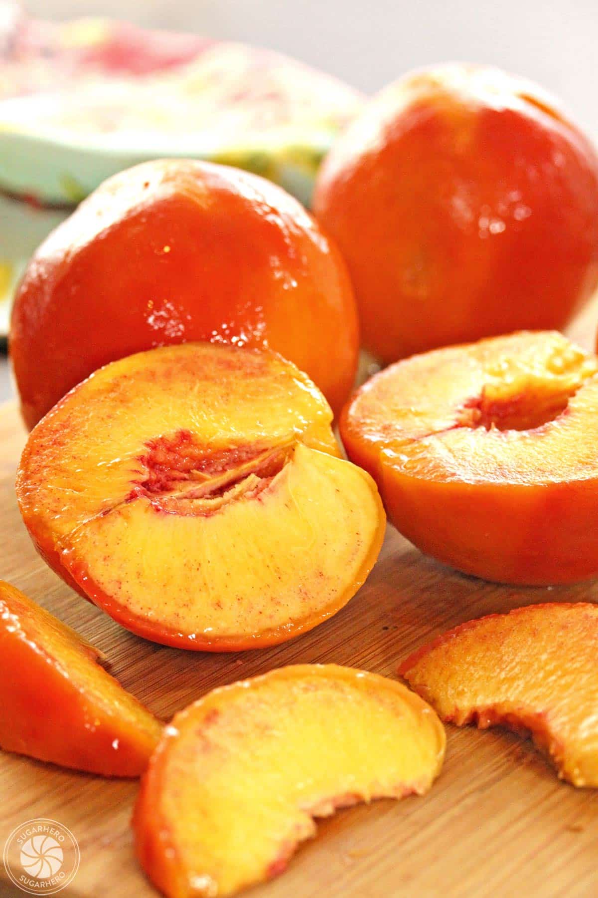 Close up of whole, halved, and sliced blanched peaches on a cutting board.
