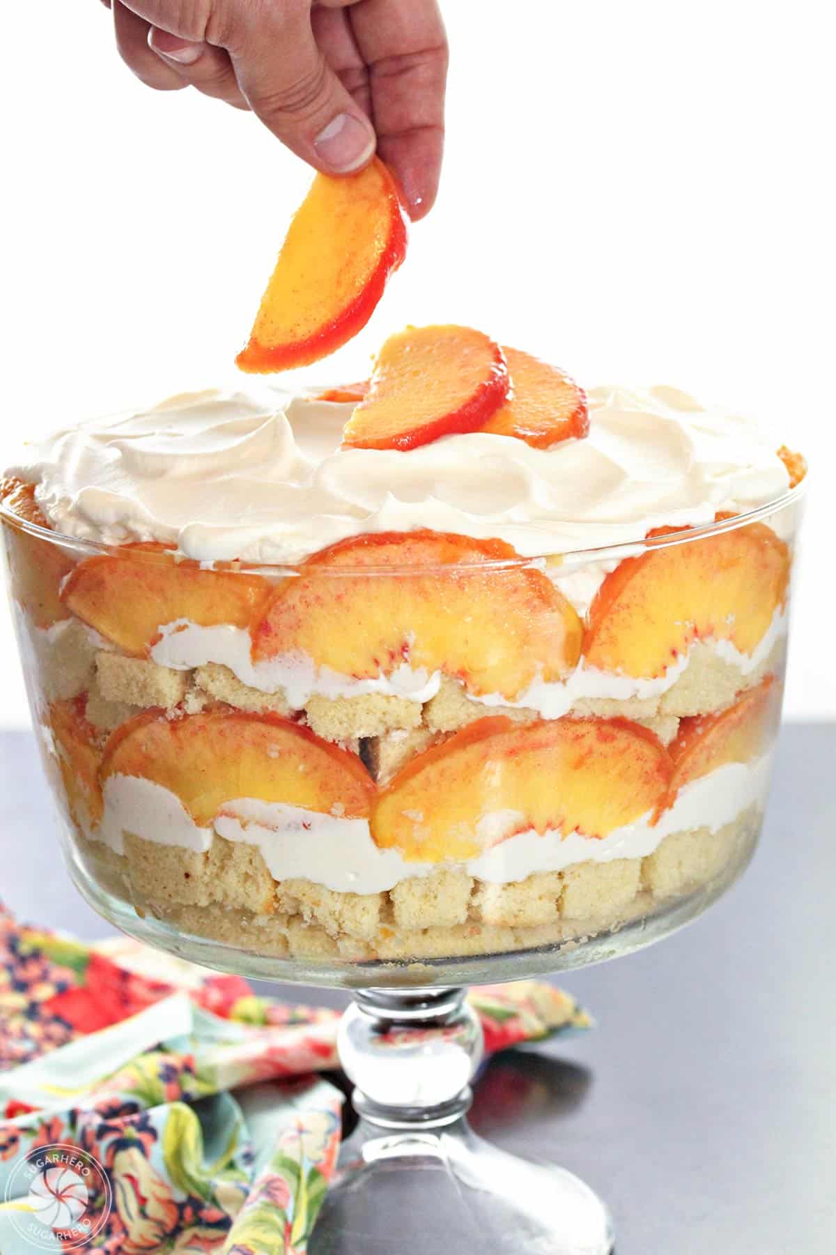 Hand placing a peach slice on top of a peaches and cream trifle.